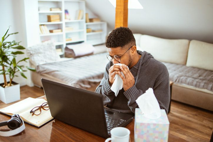 Man sneezing in front of his computer in a living room